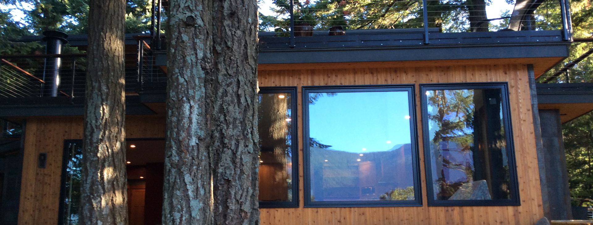Exterior of the Caldwell Private Residence, a modern custom home with natural wood siding, large windows, and a roof deck nestled in a forested setting.