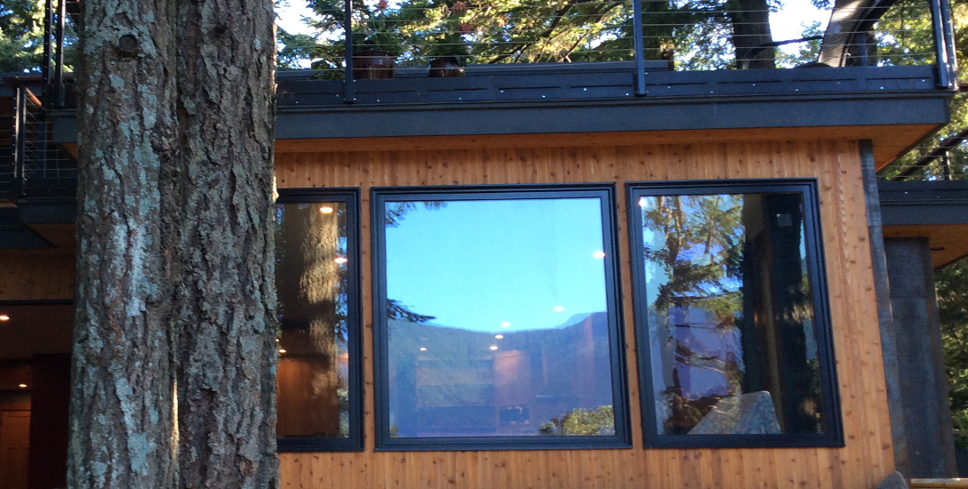 Exterior panorama of the Caldwell home showing large window panels, stacked timber textures, and the modern mountain-living design embedded in the woods.