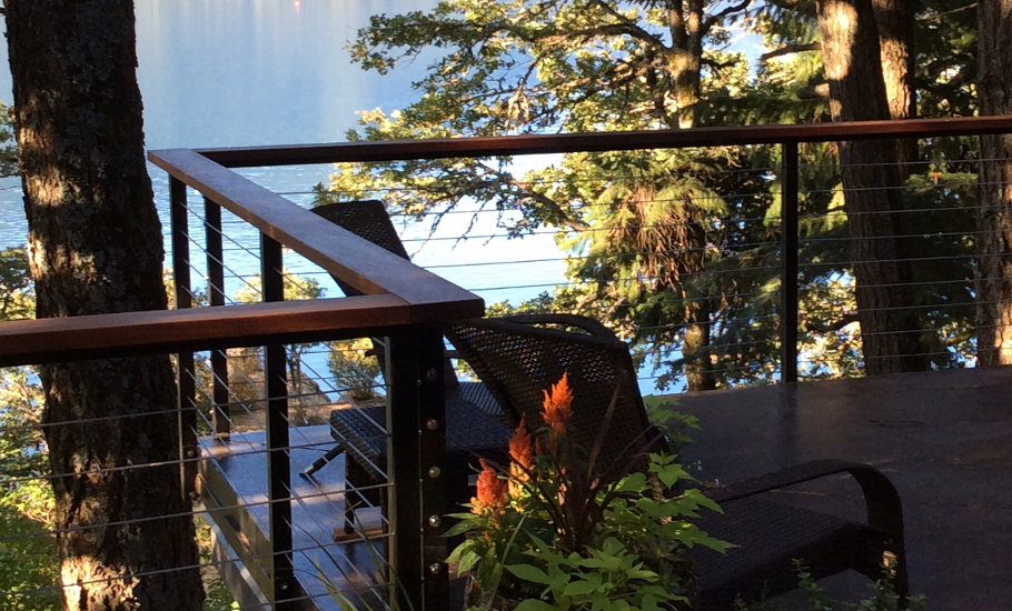 Outdoor deck seating area at the Caldwell home, with chairs, wood surfaces, and a forest backdrop that emphasizes the home’s connection to the site.