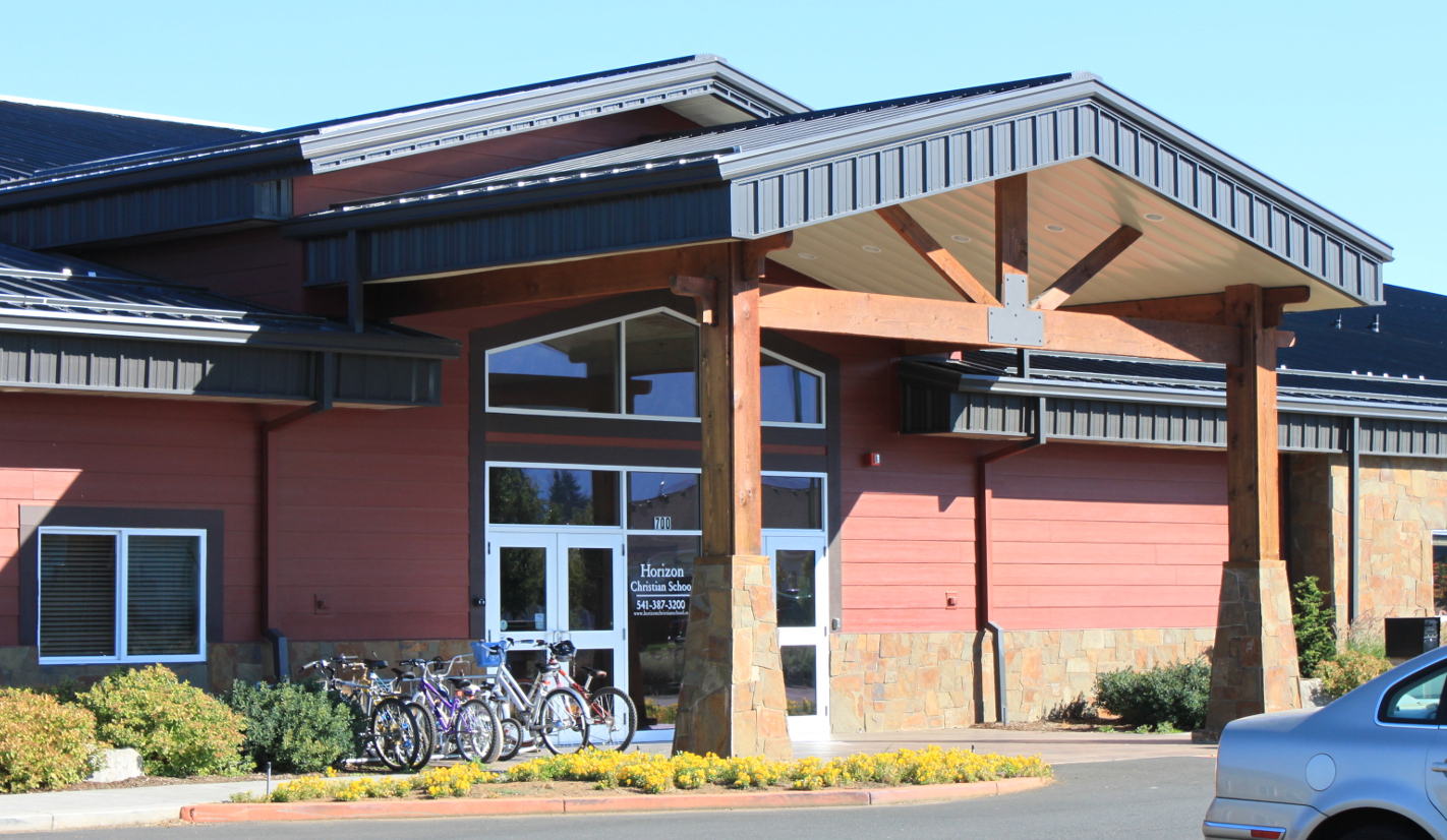 Exterior of a commercial municipal building featuring a large, exposed heavy-timber truss entrance canopy and stonework column bases.